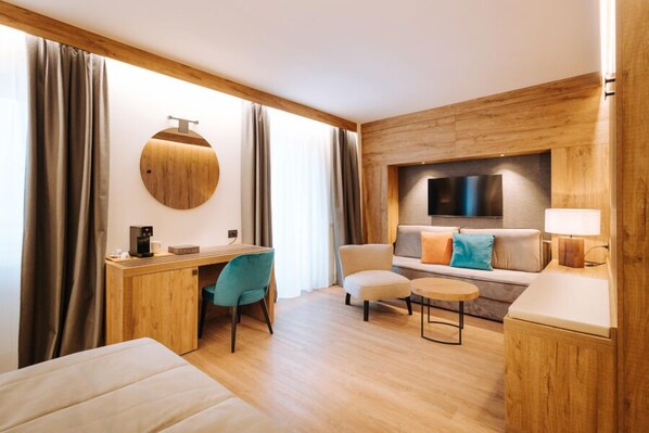 Ein modernes Hotelzimmer mit Schreibtisch aus Holz, einer bequemen Couch, einem kleinen runden Tisch und einem an der Wand montierten Fernseher.