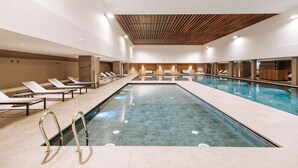 Une piscine intérieure moderne, dotée de chaises longues et d’un plafond en bois.