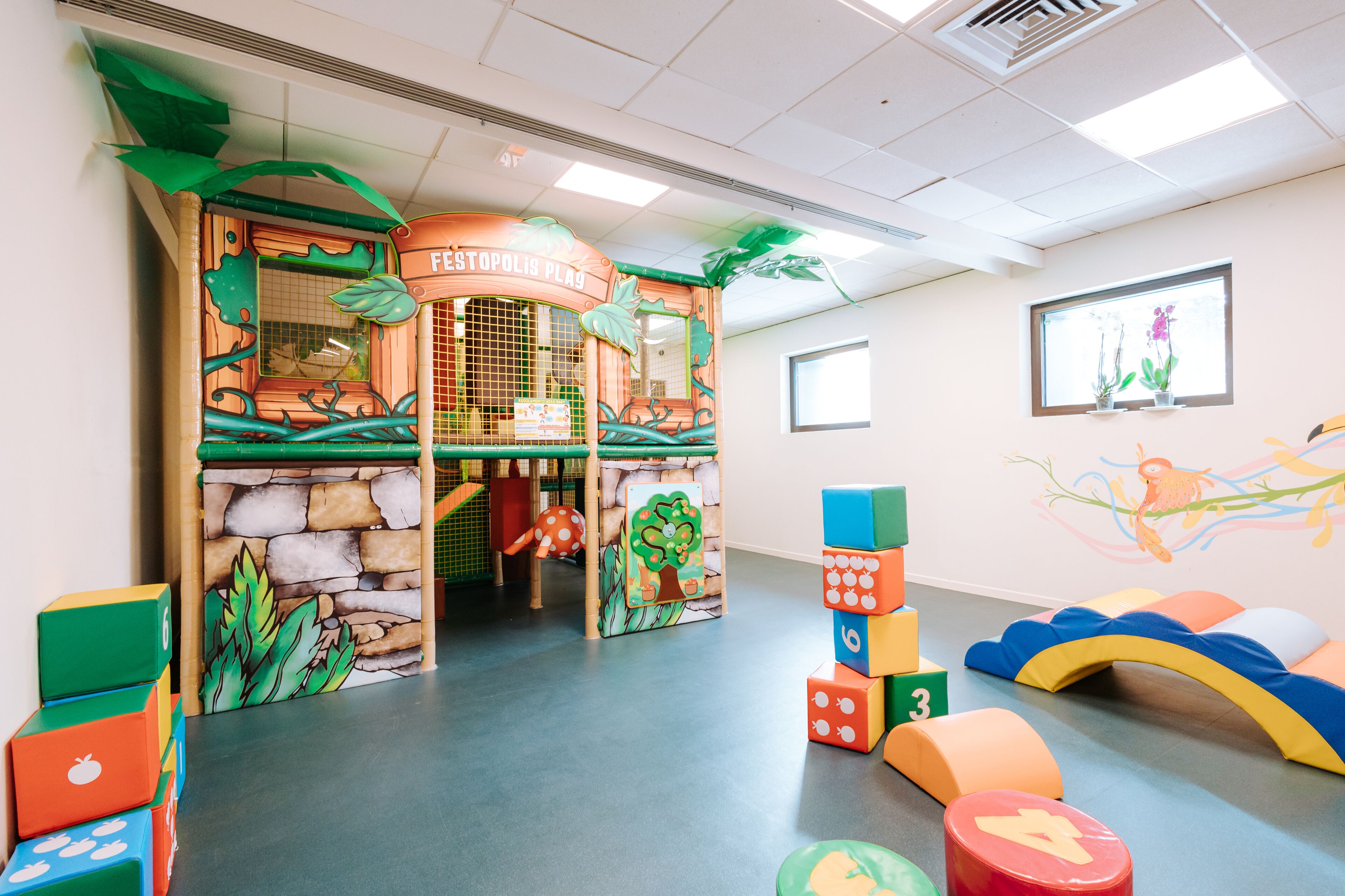 Un espace de jeux pour enfants avec une structure de jeu sur le thème de la jungle, des blocs de construction colorés et un espace de jeux doux avec des coussins.