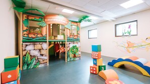 Un espace de jeux pour enfants avec une structure de jeu sur le thème de la jungle, des blocs de construction colorés et un espace de jeux doux avec des coussins.