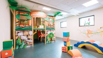 Un espace de jeux pour enfants avec une structure de jeu sur le thème de la jungle, des blocs de construction colorés et un espace de jeux doux avec des coussins.