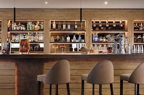 A bar area with multiple shelves of liquor bottles, a few glasses, and three bar stools. - Valtur Cervinia Cristallo Ski Resort (Valtournenche)