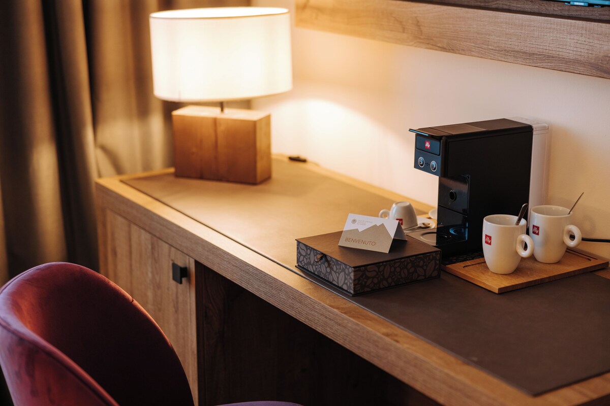A hotel room desk with a coffee maker, two mugs, a tissue box, and a lamp.