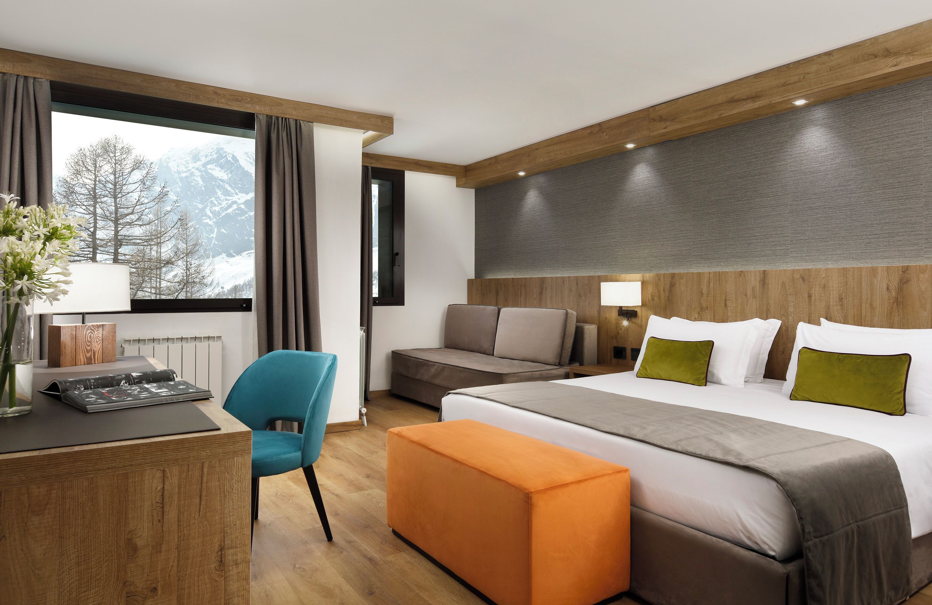 Une chambre d’hôtel avec un lit, un bureau, une chaise, un canapé et une vue sur les montagnes par la fenêtre.