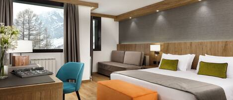 Une chambre d’hôtel avec un lit, un bureau, une chaise, un canapé et une vue sur les montagnes par la fenêtre.