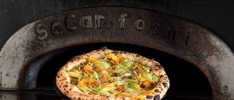 Une pizza cuite dans un four en briques, sur la porte duquel on peut lire l’inscription « Sacarforni ».
