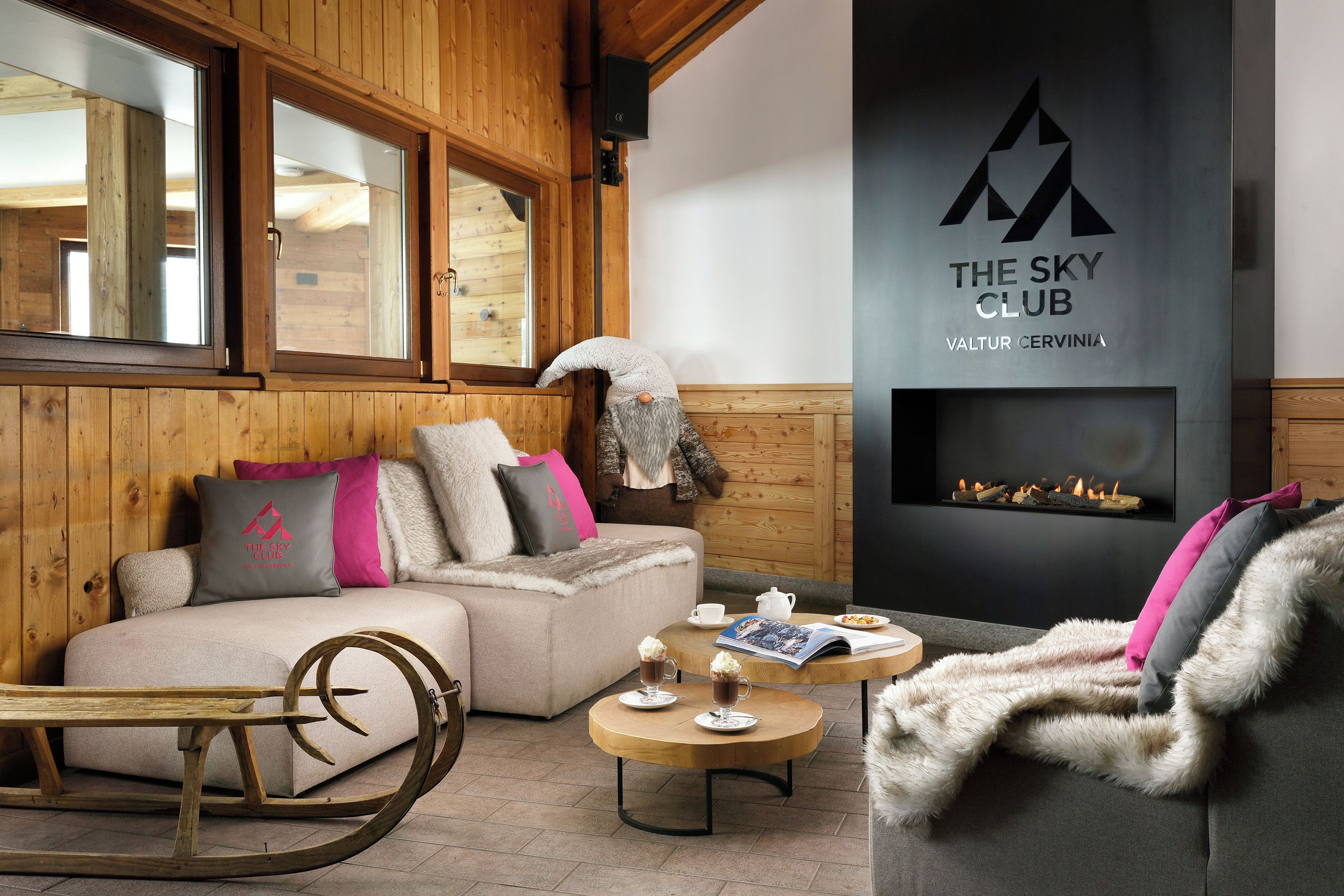 A cozy room with a sofa, a wooden rocking chair, a fireplace, and a large window.