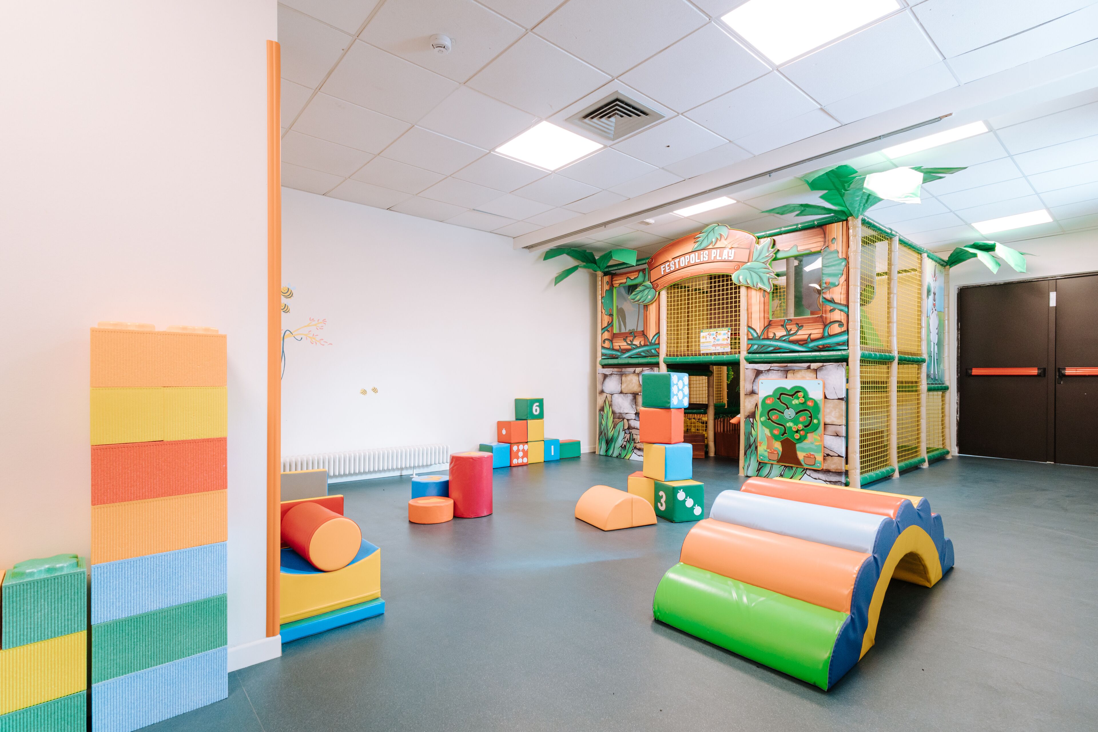 Un espace de jeux avec des blocs de mousse colorés, une maison de jeux et des structures de jeux en matériaux souples.