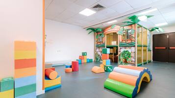 Un espace de jeux avec des blocs de mousse colorés, une maison de jeux et des structures de jeux en matériaux souples.