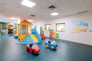 Ein Kinderspielbereich mit Rutsche, Kletterwand und bunten Spielgeräten.