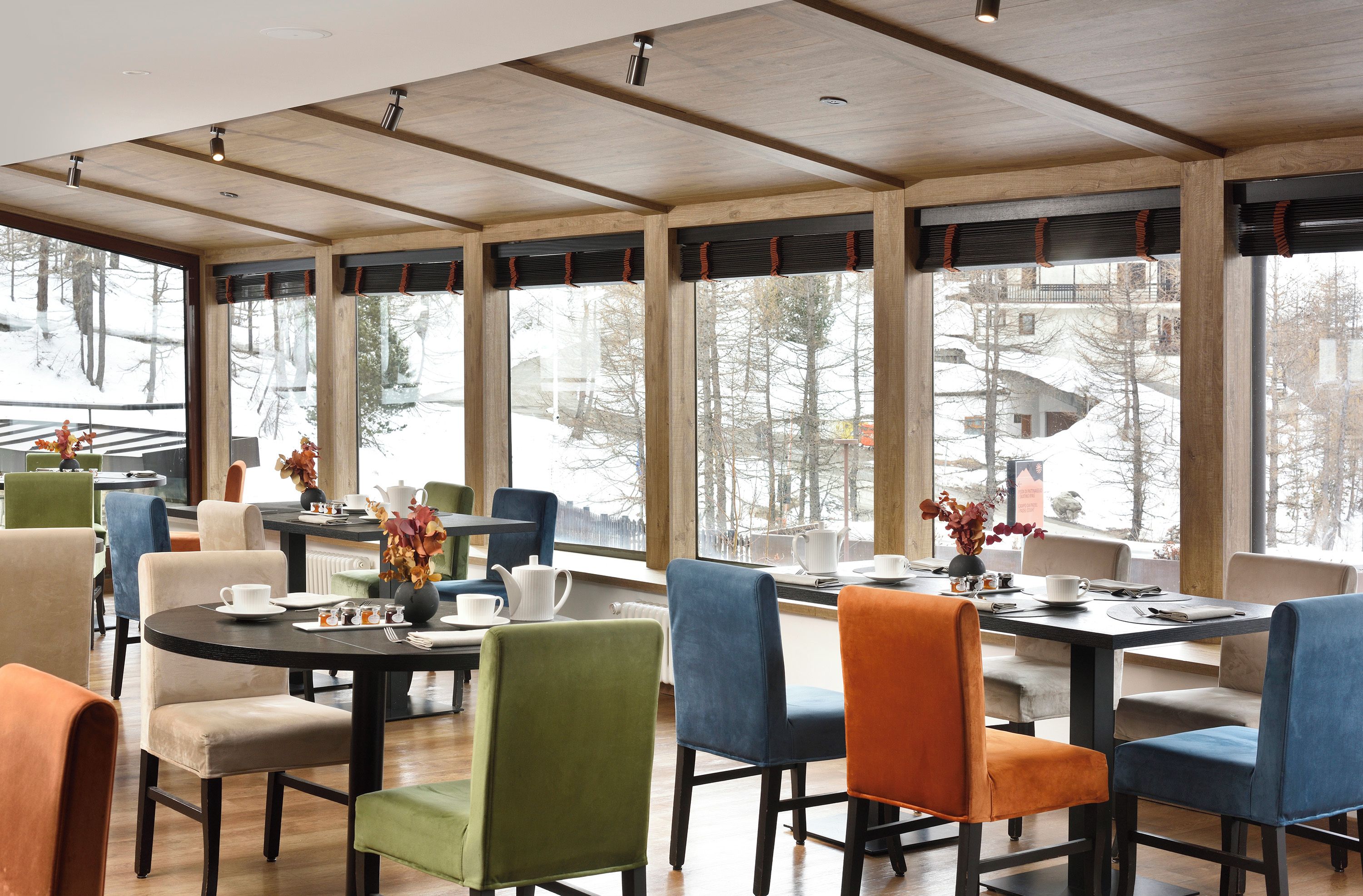 Un espace repas comprenant plusieurs tables et chaises, de grandes fenêtres offrant une vue sur un paysage enneigé et un plafond en bois.