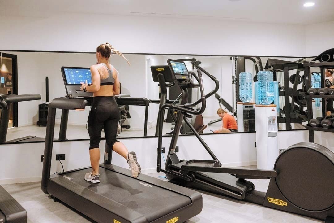 Une salle de sport équipée de tapis de course, d’appareils de musculation et d’un mur recouvert de miroirs.