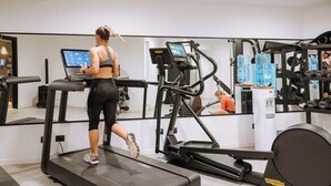 Une salle de sport équipée de tapis de course, d’appareils de musculation et d’un mur recouvert de miroirs.
