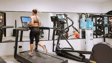 Une salle de sport équipée de tapis de course, d’appareils de musculation et d’un mur recouvert de miroirs.