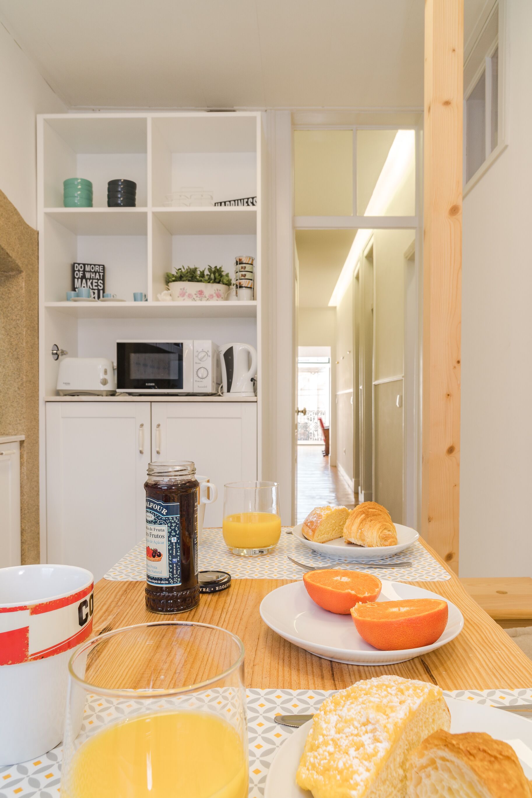 A breakfast setup with a plate of croissants, orange juice, and a jar of jam on a wooden table.