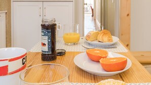 A breakfast setup with a plate of croissants, orange juice, and a jar of jam on a wooden table.