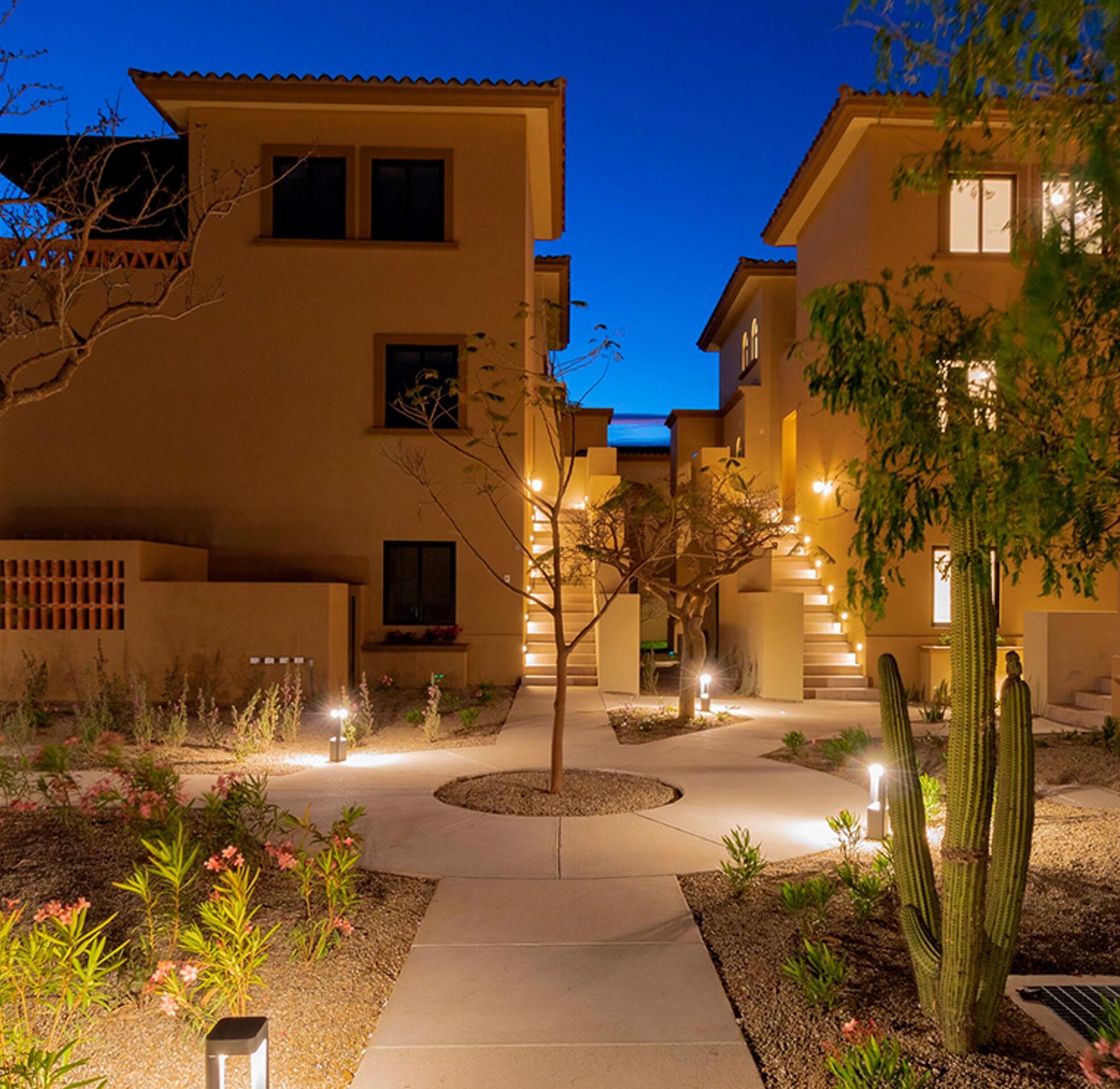 A residential area with multiple two-story houses, a central pathway, and landscaped gardens with cacti and flowering plants.