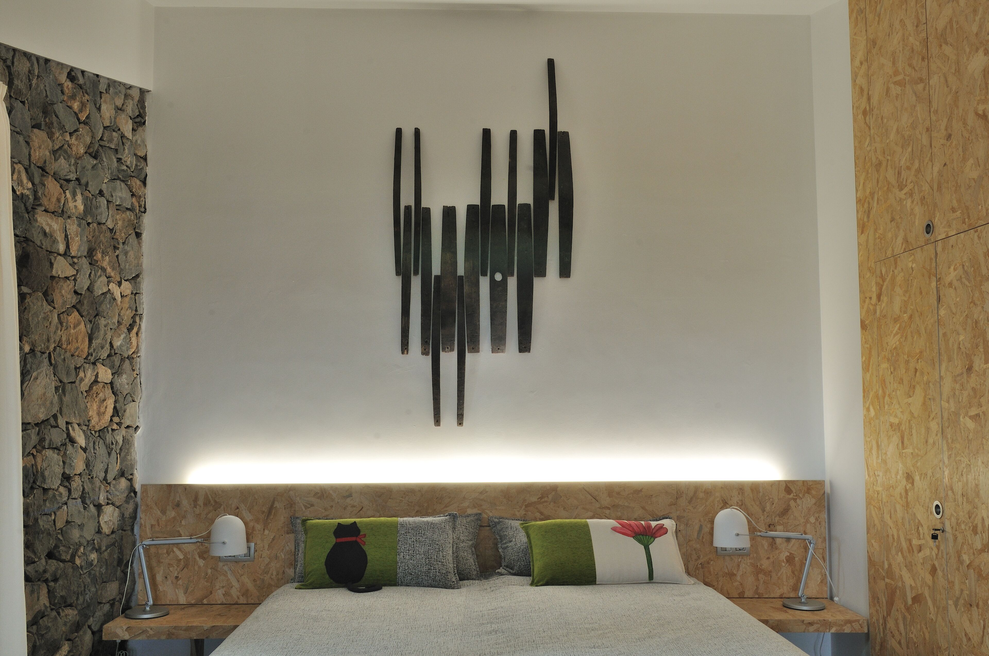 A modern bedroom with a stone accent wall, a wooden headboard, and a minimalist abstract art piece above the bed.