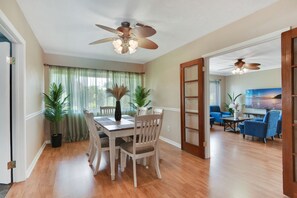 Enjoy meals in this dining area with a wooden table and matching chairs, surrounded by a large window and a potted plant.