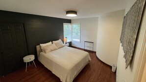 A bedroom with a bed, a nightstand, a window, and a door. - The Gaard House (Carlton)