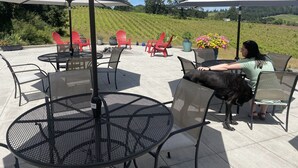 An outdoor patio with round tables and chairs, umbrellas, and a view of a vineyard. - The Gaard House (Carlton)