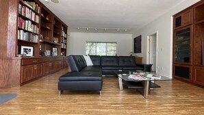 A modern living room with a black leather sofa, a glass coffee table, and a wooden bookshelf. - The Gaard House (Carlton)