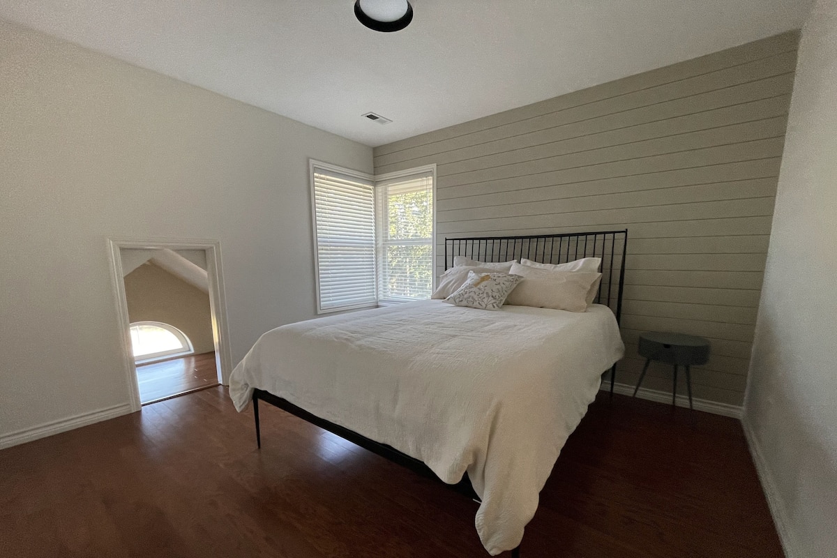 A bedroom with a bed, a small table, and a window with blinds.