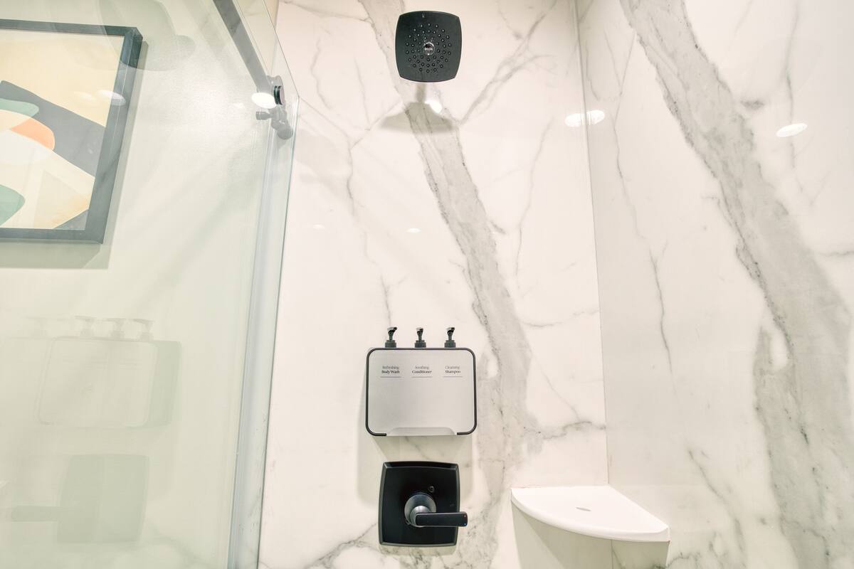 Un baño con pared de mármol, cabezal de ducha, dispensador de jabón y un inodoro.