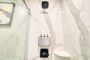 Ein Badezimmer mit Marmorwand, Duschkopf, Seifenspender und Toilette.