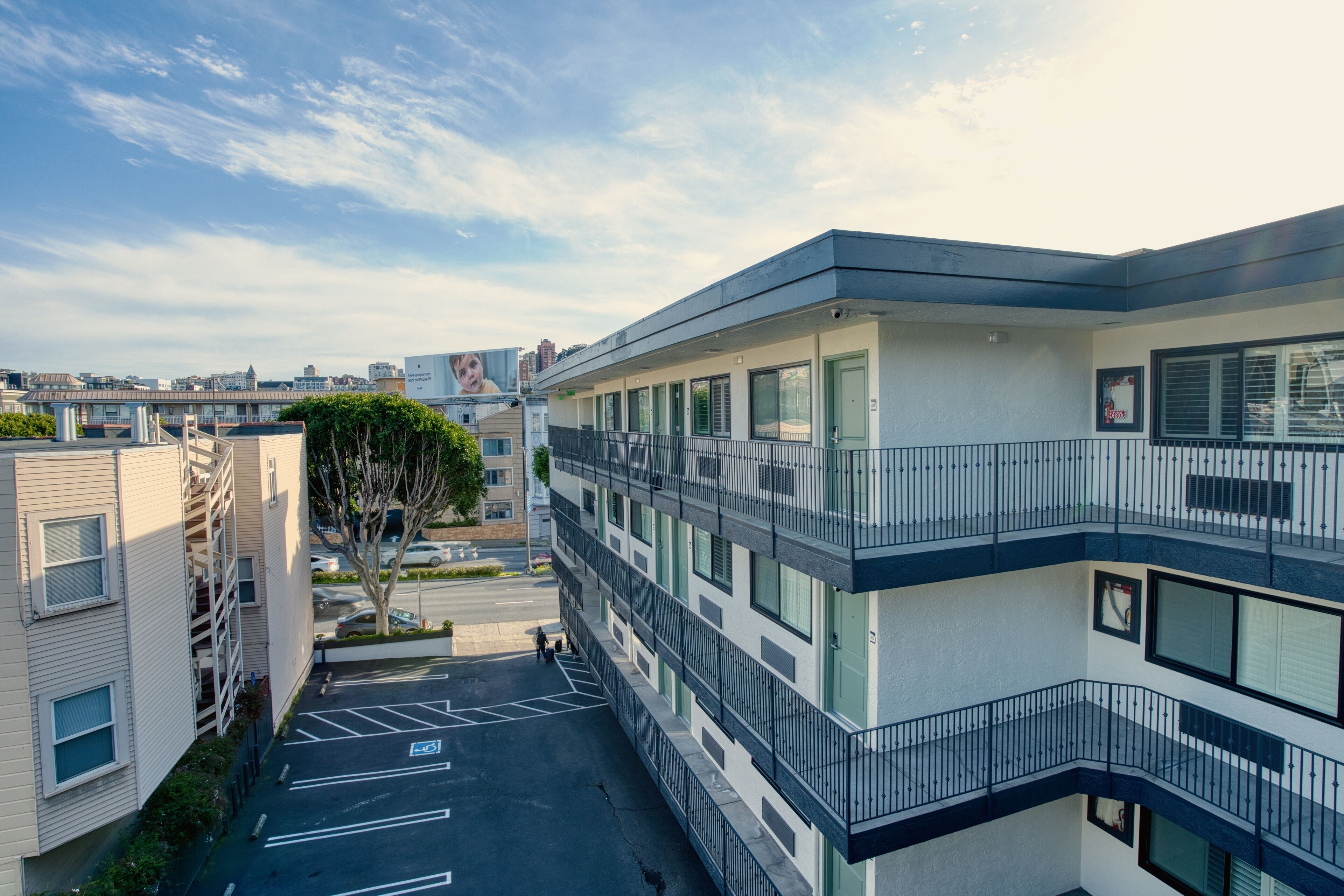 A multi-story building with a parking lot, a tree, and a clear sky.