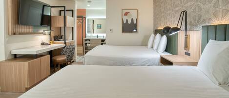 A hotel room with two beds, a desk, a chair, a TV, and a wall with a geometric pattern.