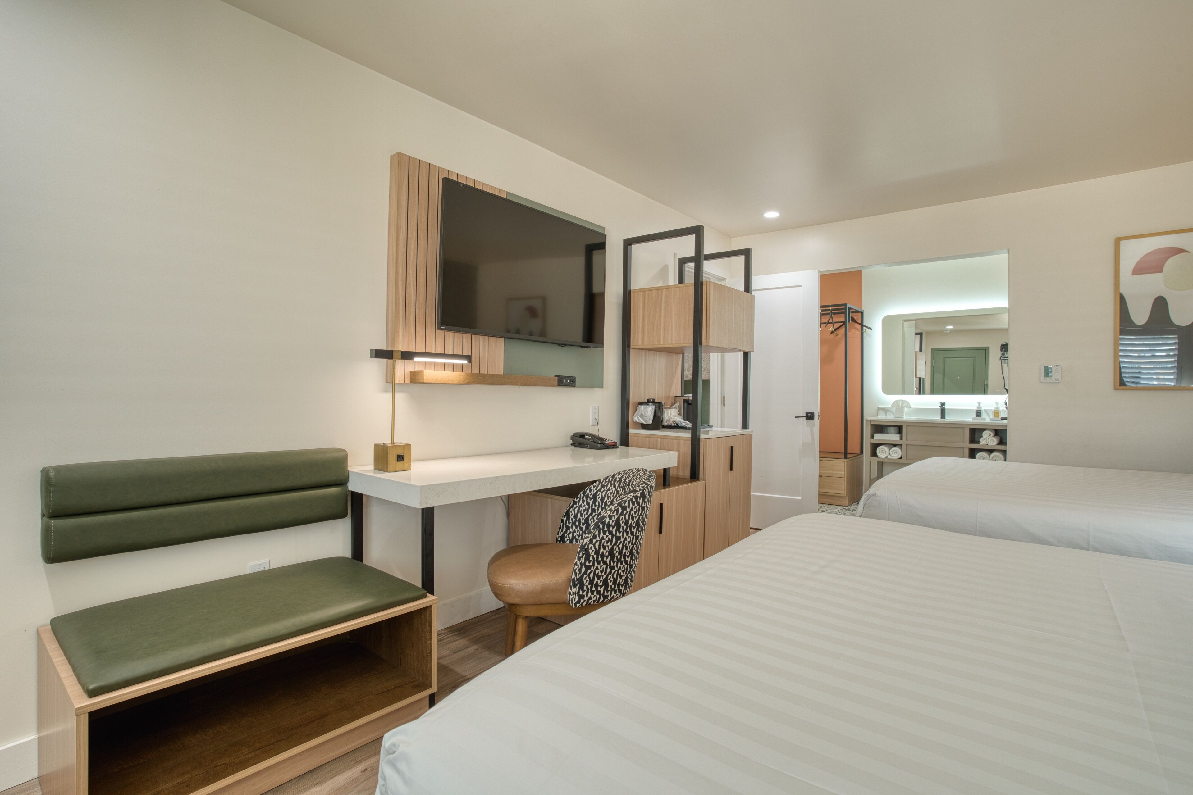 Una habitació d'hotel moderna amb escriptori, una banca amb coixí verd, un llit individual i un mirall gran.
