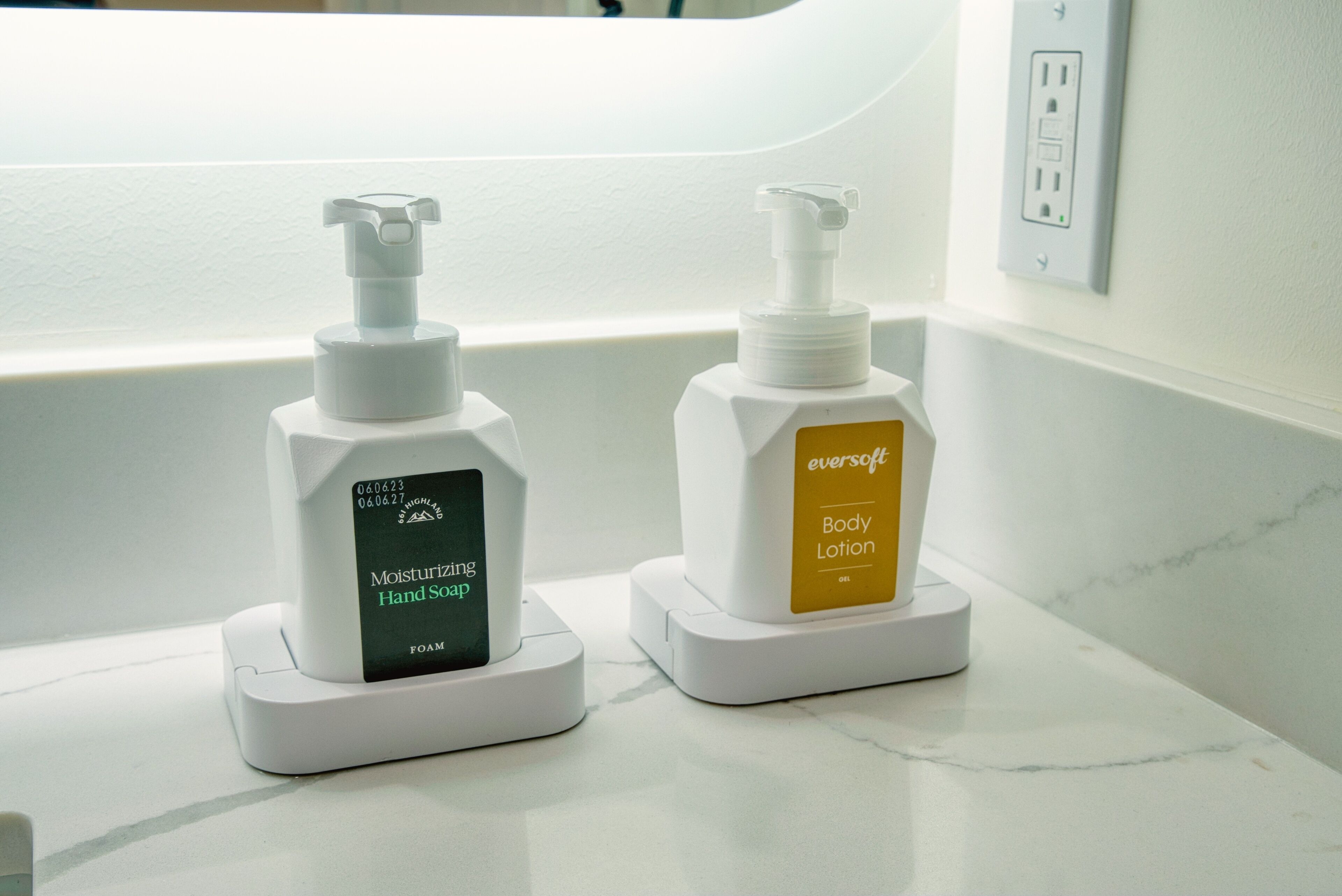 Two hand soap dispensers on a white countertop near a wall socket.