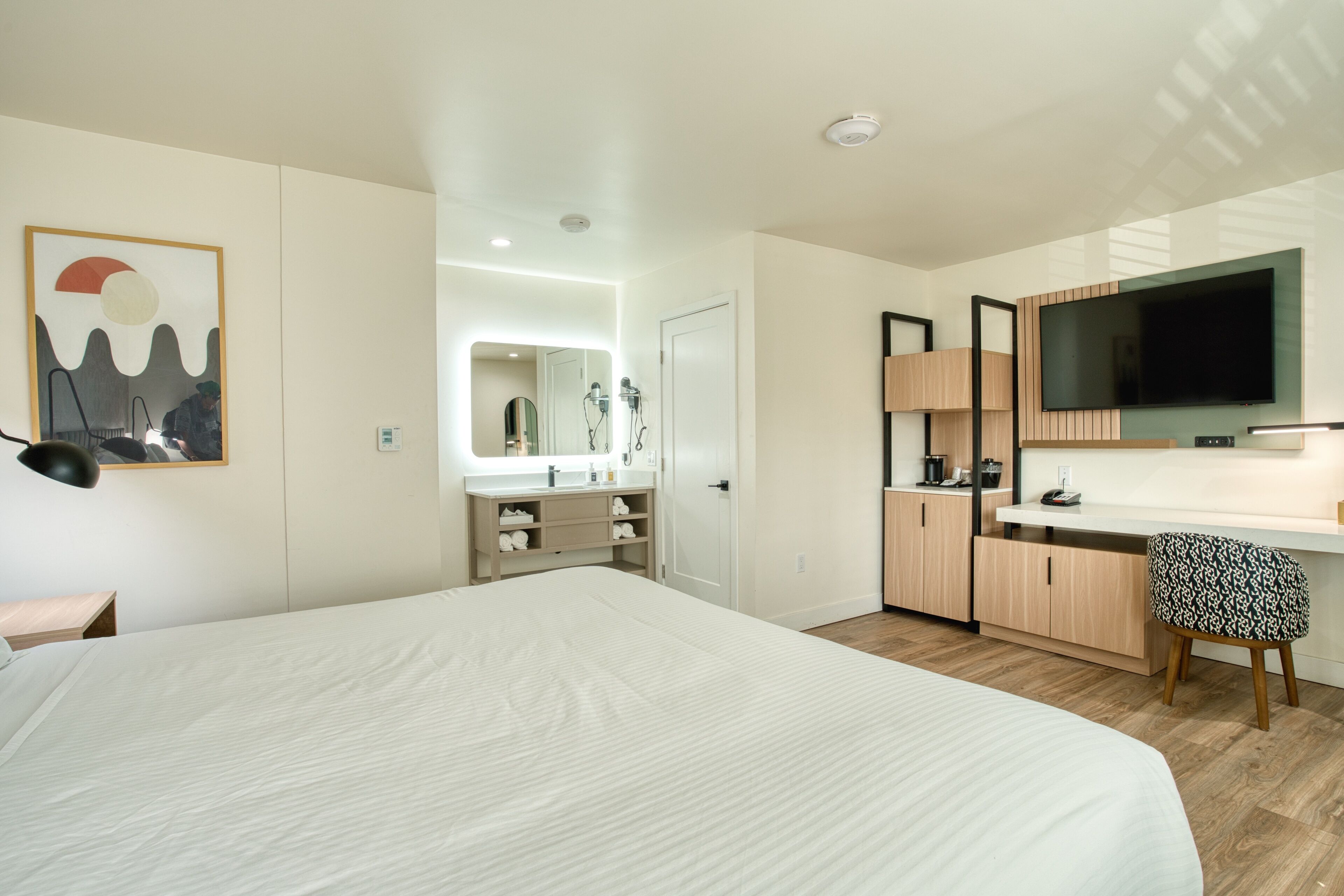 A modern hotel room with a large bed, a desk, a television, and a bathroom with a mirror and sink.