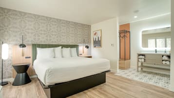 A modern bedroom with a large bed, a bedside table, a floor lamp, a mirror, and a wardrobe.