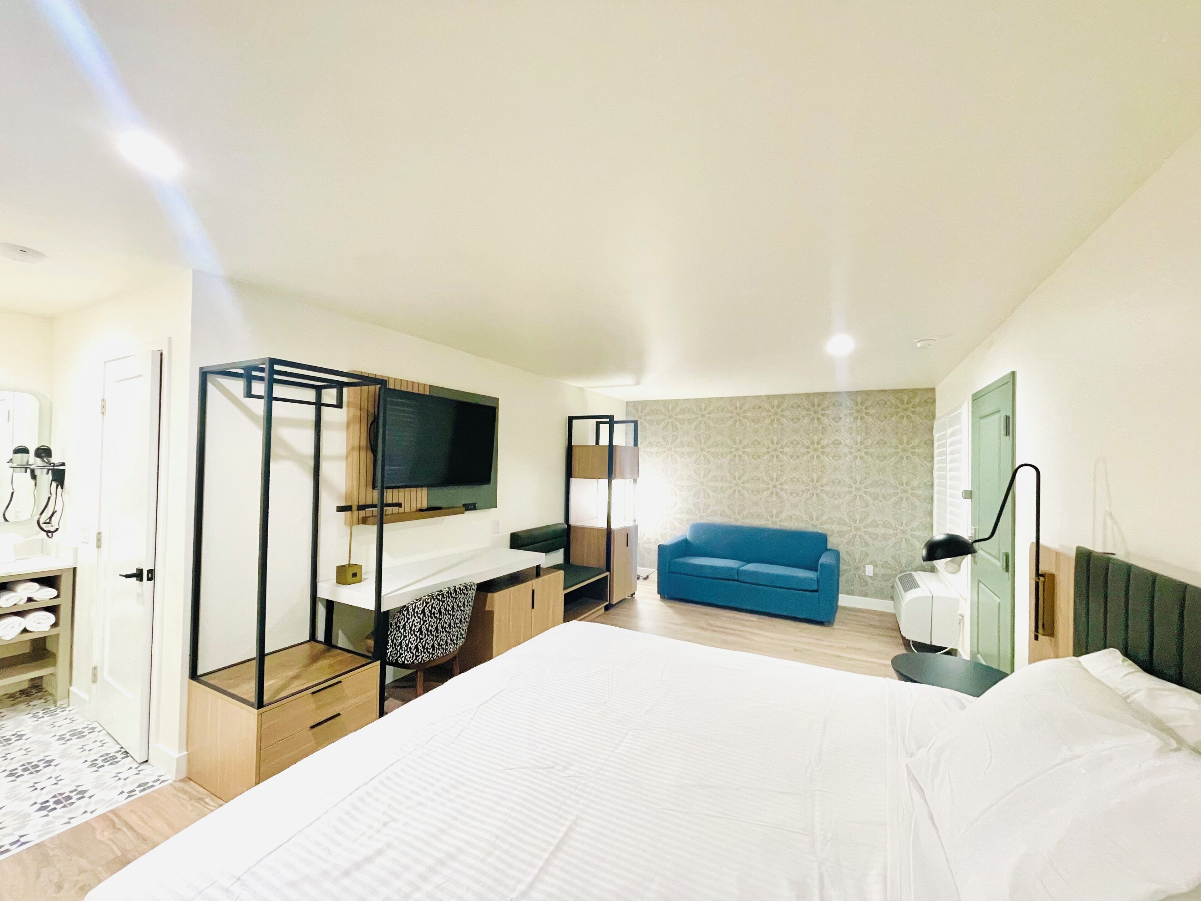 A modern hotel room with a large bed, a TV mounted on the wall, a blue sofa, and a wardrobe.