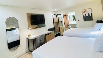 Habitación de hotel con una cama grande, un escritorio con silla, un televisor, un espejo y un ventanal pequeño.
