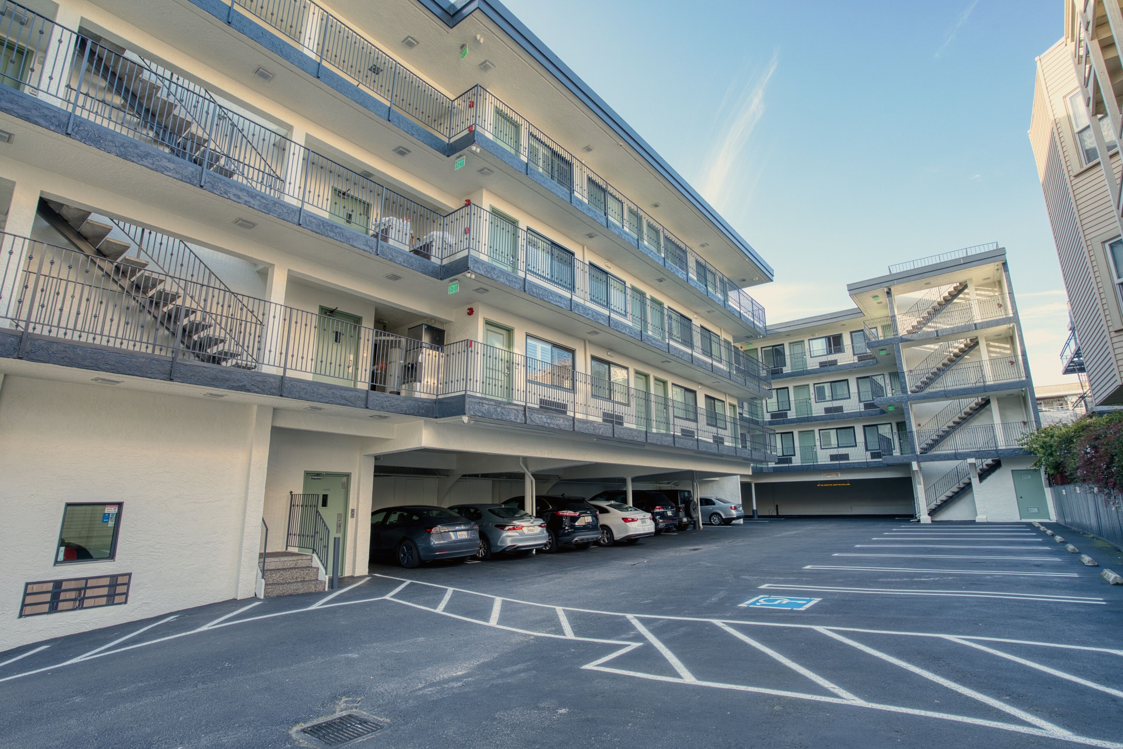 A multi-story parking garage with several cars parked, a stairway leading to the upper floors, and a clear sky above.