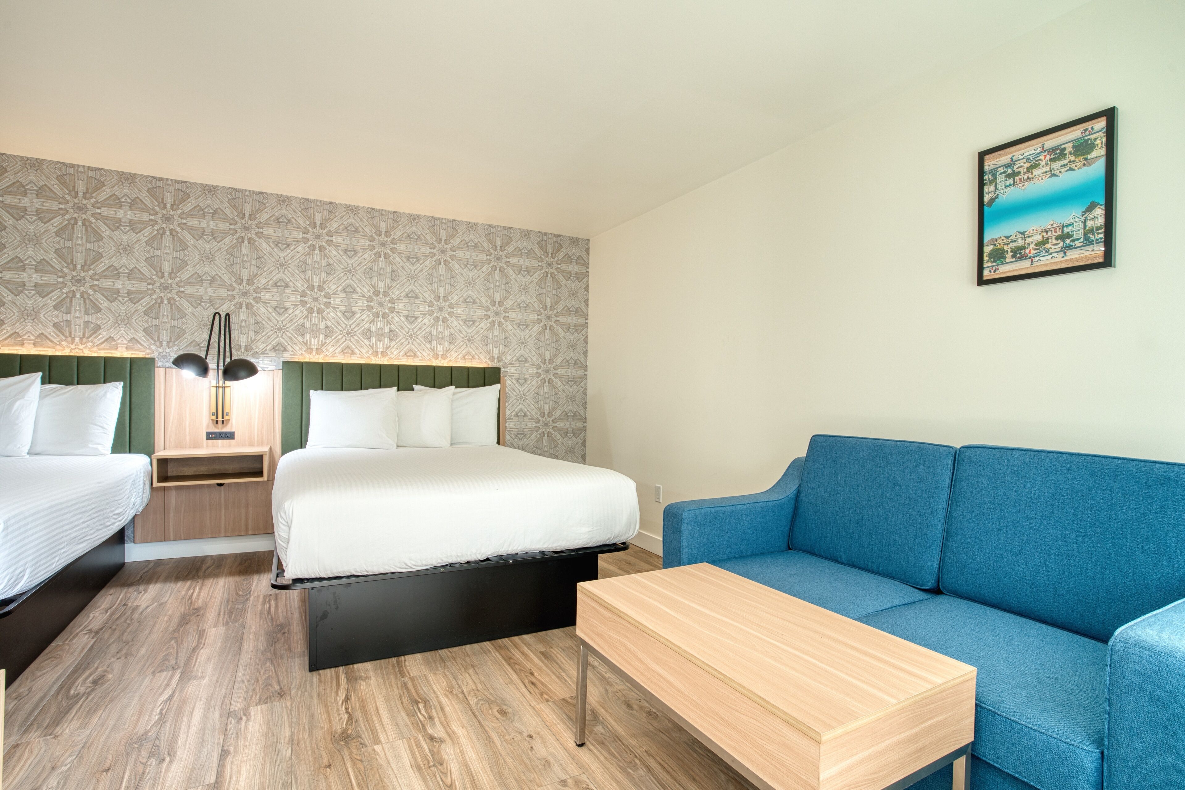 Habitación de hotel con dos camas, un sofá azul, una mesa de madera y una pared con diseño.