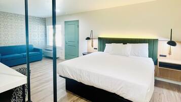 A modern bedroom with a large bed, a blue sofa, and a mirrored wardrobe.