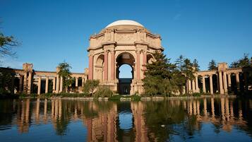 A large, classical building with a central dome and arched entrance, surrounded by a reflective water body and trees.
