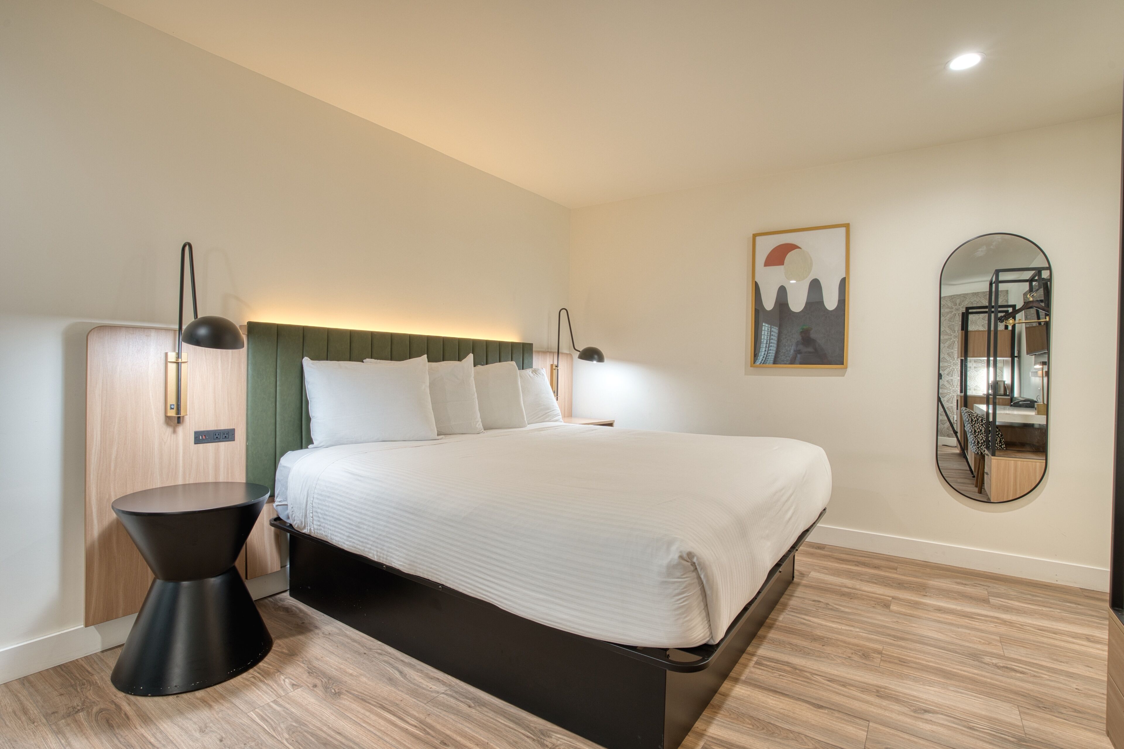 A modern bedroom with a large bed, a round mirror, and a bedside table.