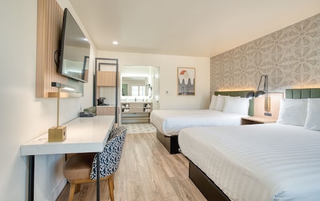A hotel room with two beds, a desk, a chair, a TV, and a bathroom visible through an open door.