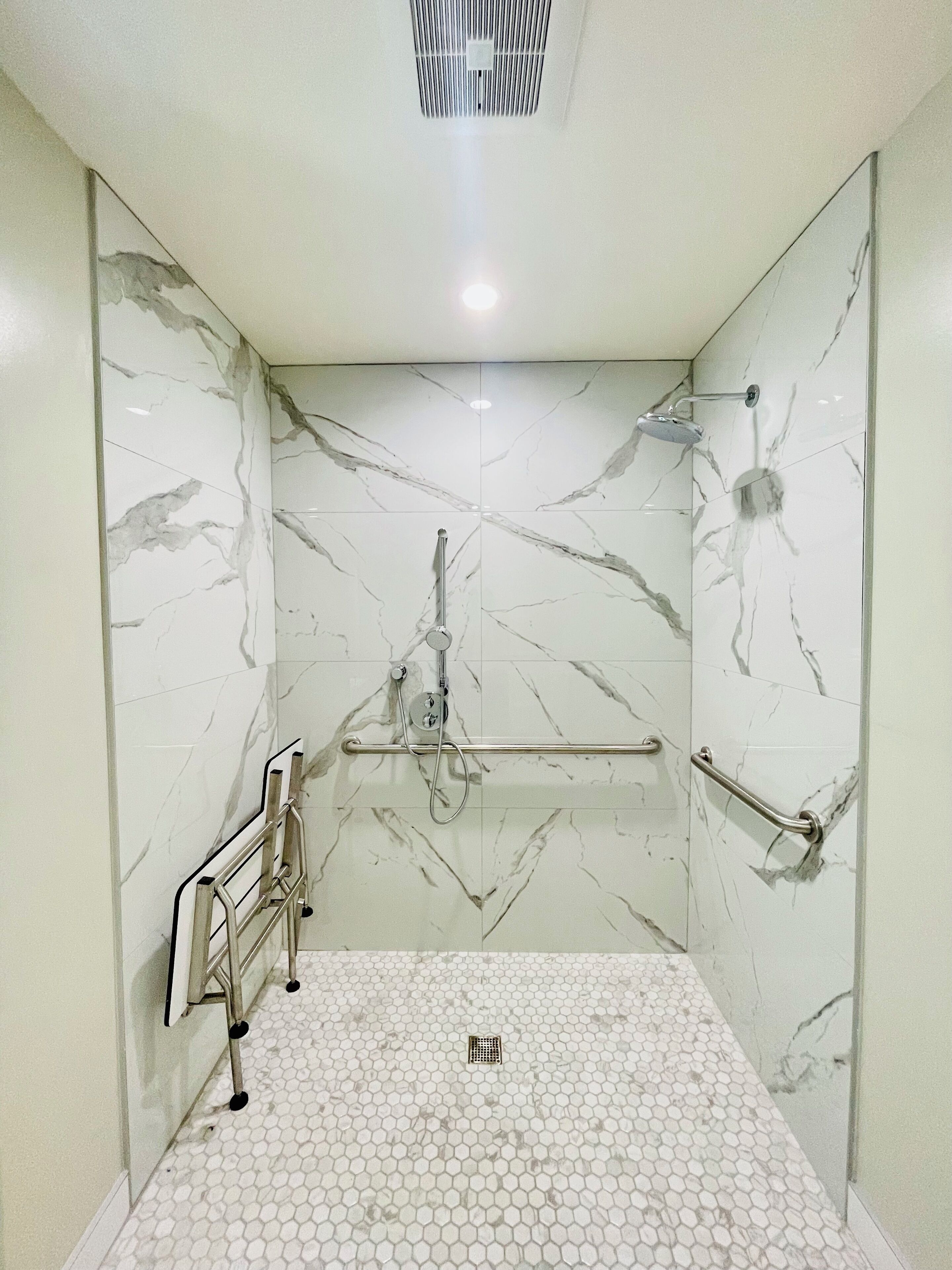 Un bagno con pareti e pavimento in marmo, una doccia con soffione a mano e una barra di sostegno.