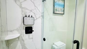 A modern bathroom with a glass-enclosed shower, a toilet, and a marble wall.