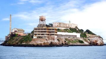 Ein historischer Gebäudekomplex mit mehreren Bauten, darunter ein markanter Turm und ein großer Wasserturm, auf einer felsigen Insel mit Blick auf das Meer.