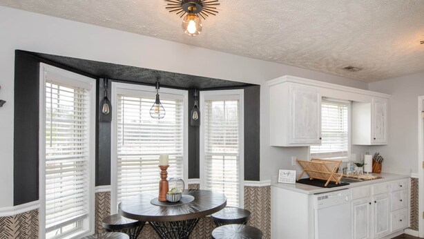 A dining area with a round table and six chairs, a kitchen with white cabinets, and a herringbone-patterned wall. - The Herringbone Blue (Harnett County)