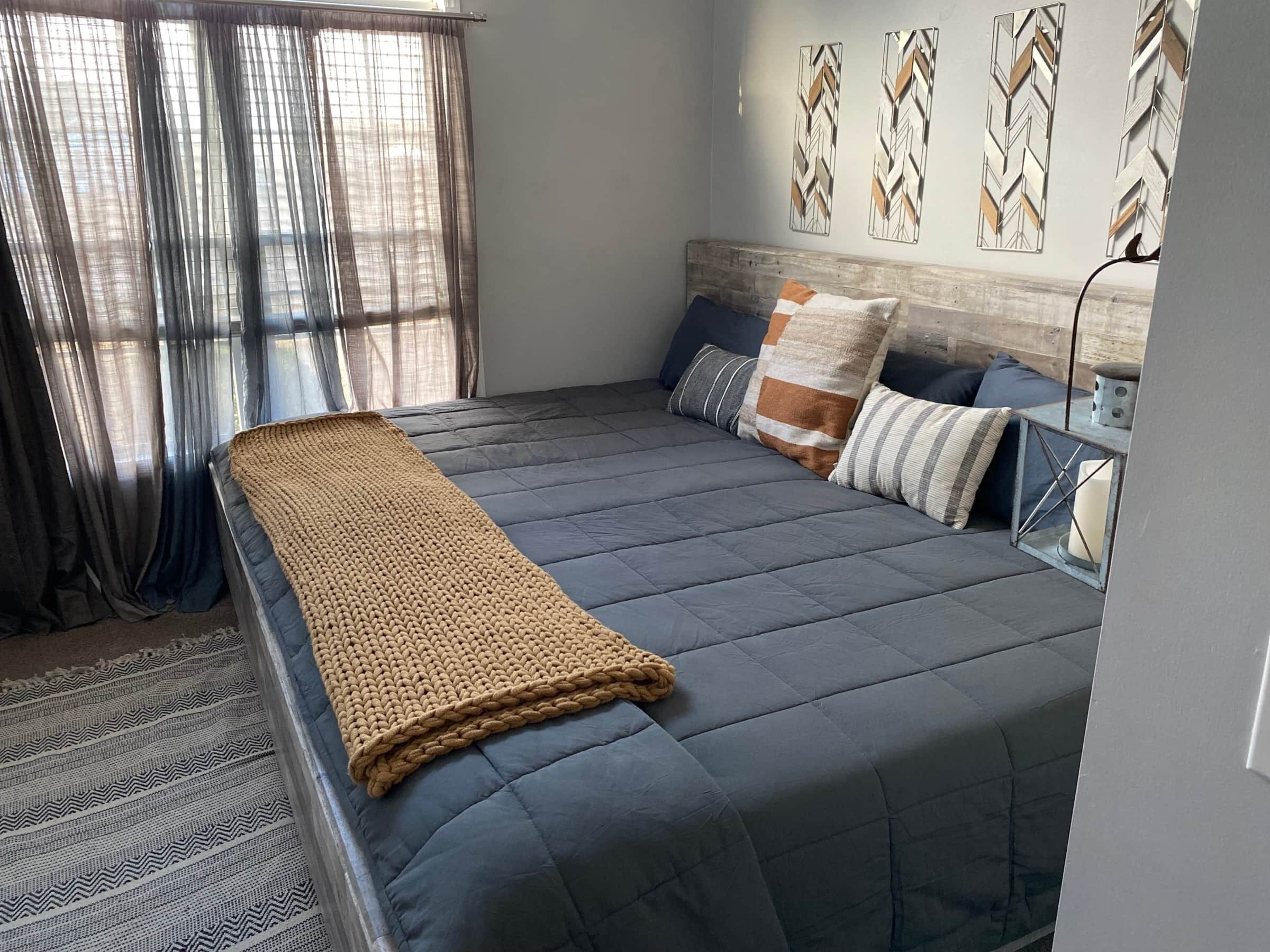 A neatly made bed with a grey duvet, a beige knitted throw, and several pillows.