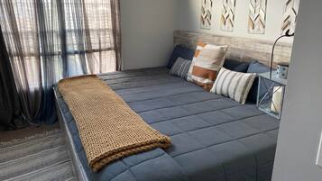 A neatly made bed with a grey duvet, a beige knitted throw, and several pillows.