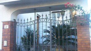 Une entrée fermée par un portail, agrémentée d’un panneau indiquant un numéro, d’un mur en briques et d’un portail en métal orné d’éléments décoratifs.